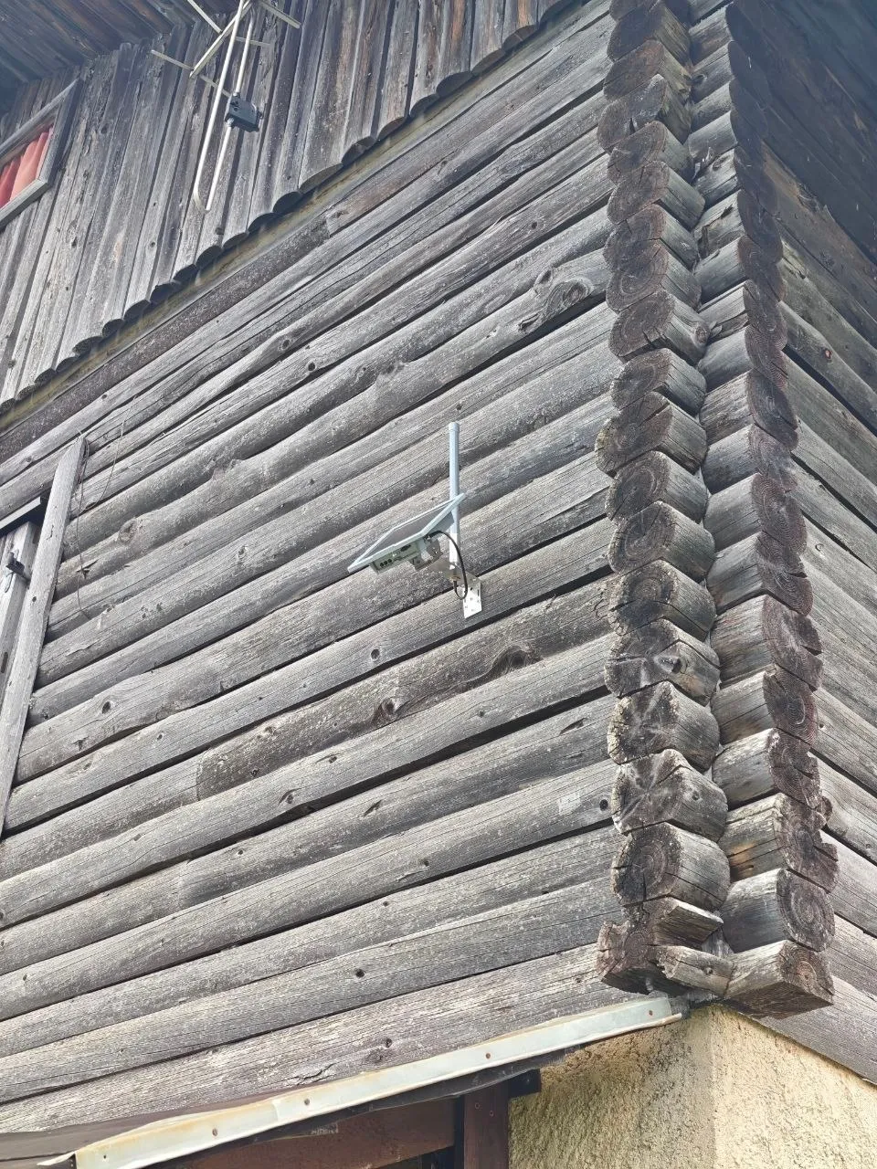 Solar-Node mit kleinem Panel und Antenne an der verwitterten Blockwand der Almhütte