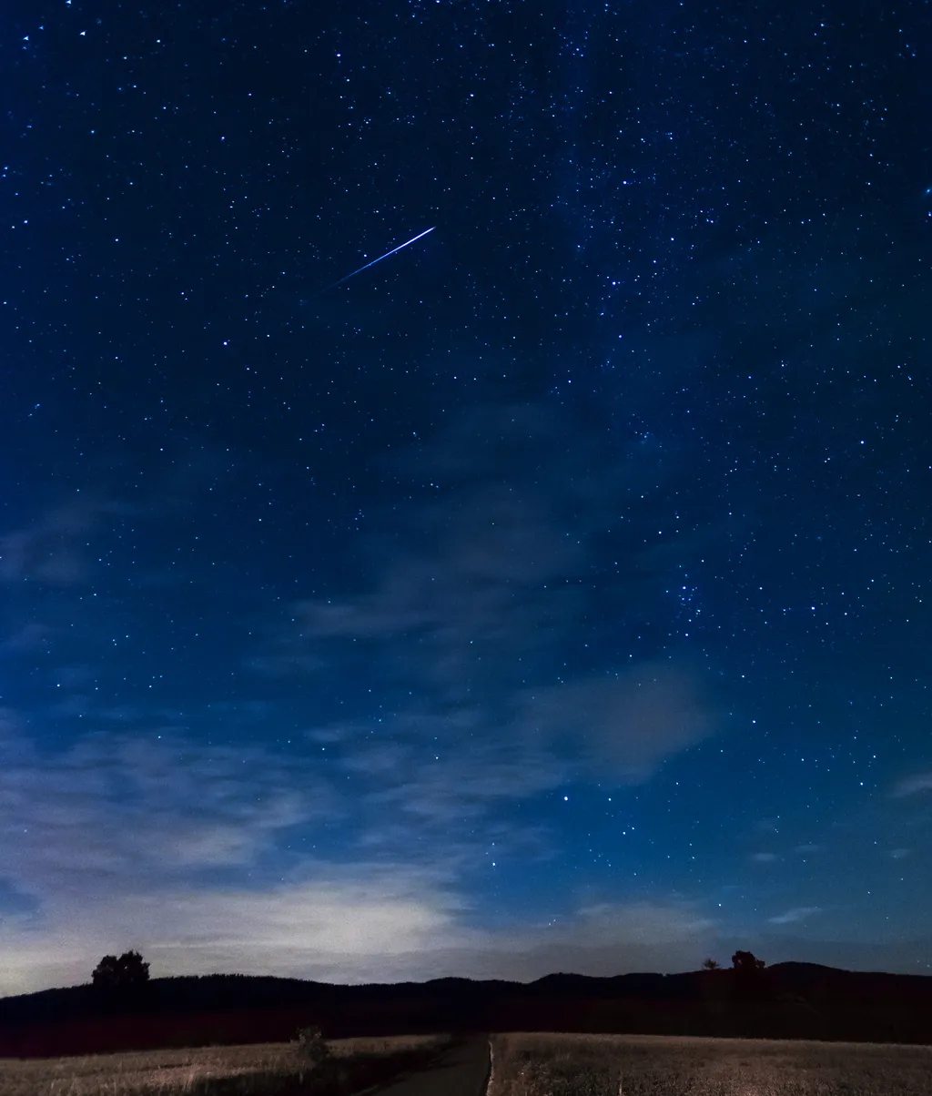 Heller Meteor am Nachthimmel über einer Landschaft