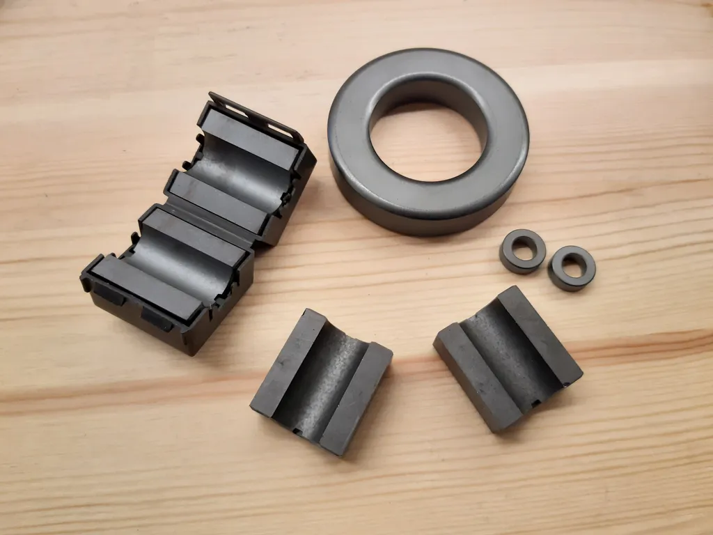 Nuclei di ferrite assortiti: un grande toroide, toroidi piccoli e ferriti a clip su una superficie di legno