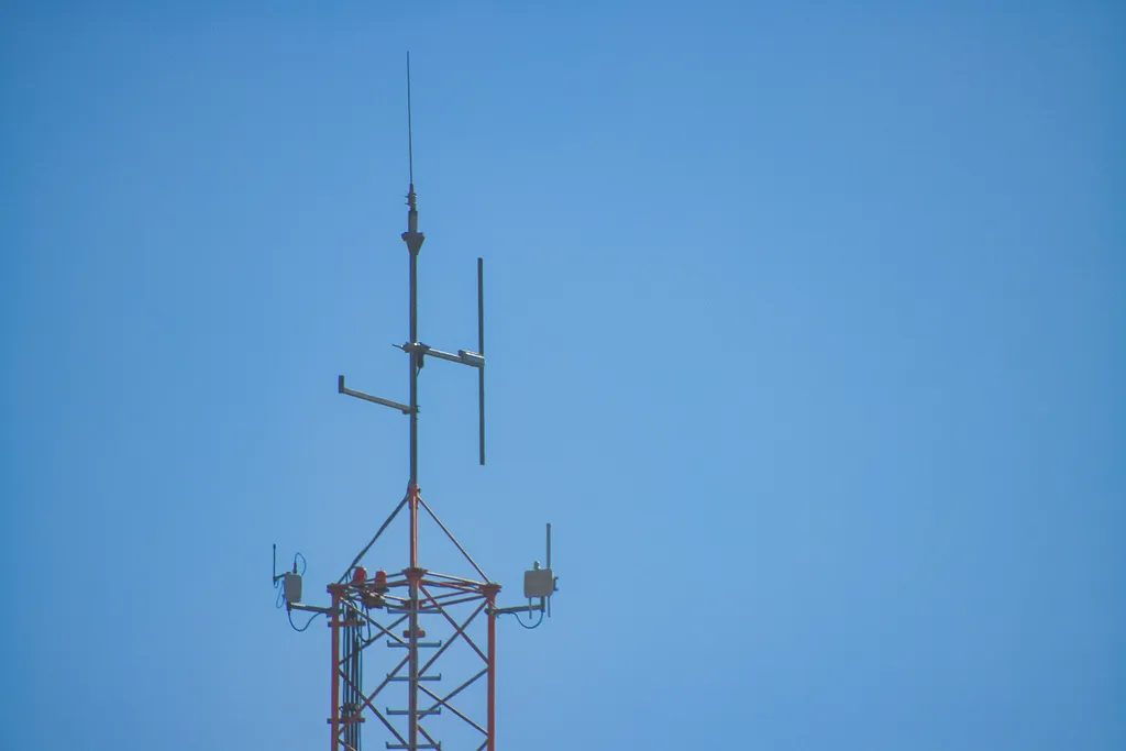 Gittermast mit LoRa-Gateways, Rundstrahlantennen und Blitzfangstange vor blauem Himmel