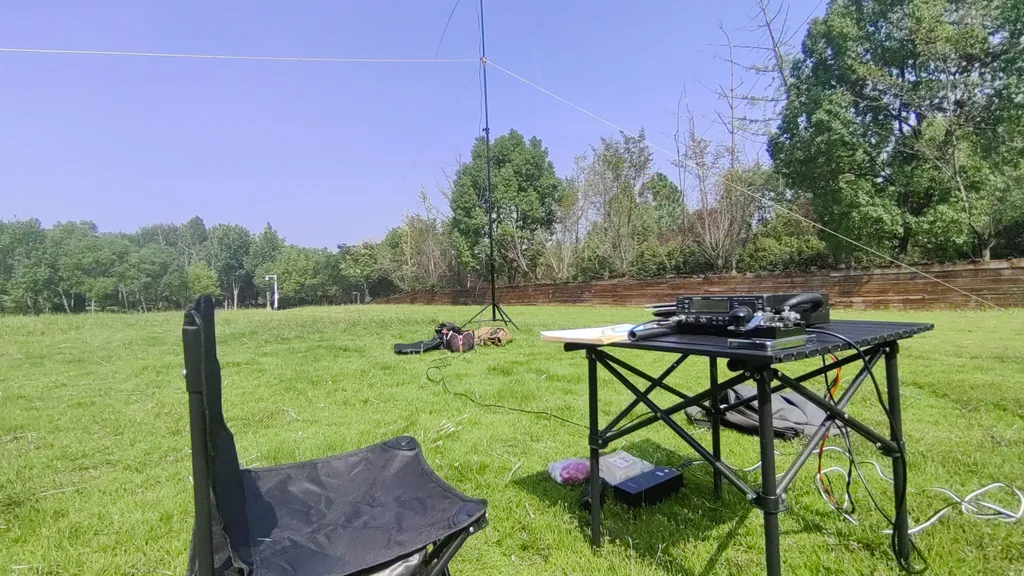 Portable POTA-Station im Park: Transceiver auf einem Klapptisch, Vertikalantenne mit Abspannungen auf der Wiese