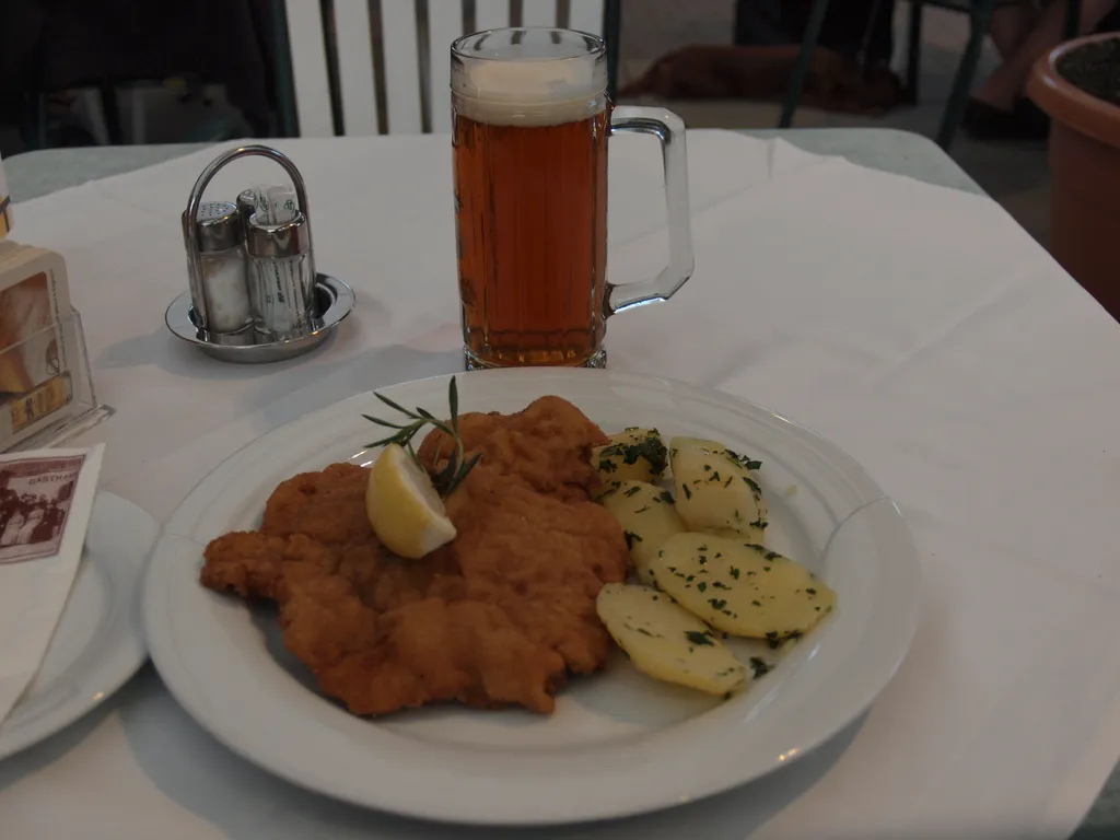 Cotoletta alla viennese con patate al prezzemolo e un boccale di birra su una tovaglia bianca da osteria