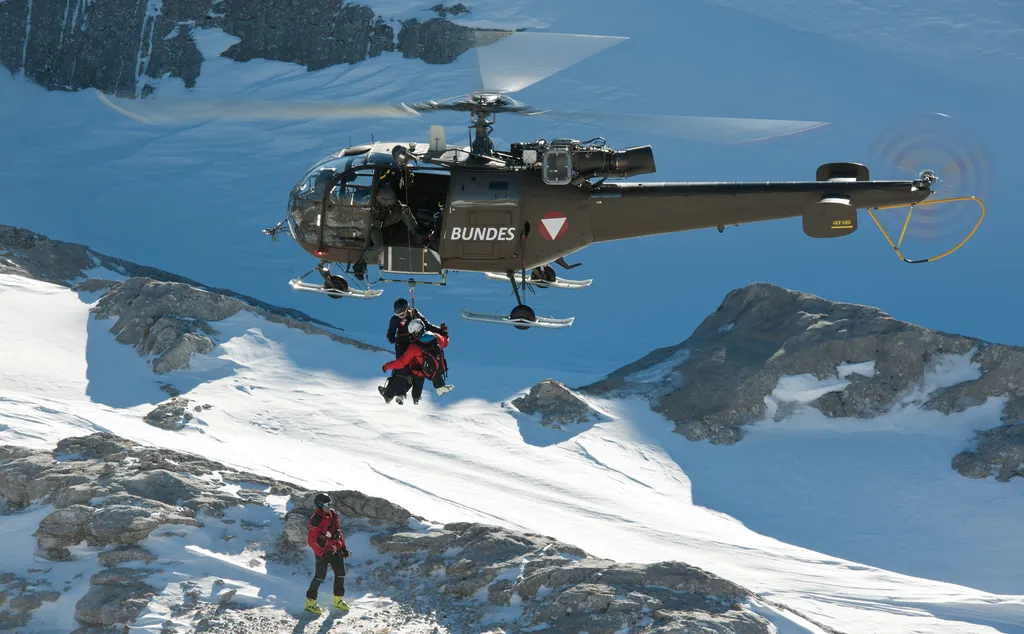 Hubschrauber des Bundesheeres mit Seilwinde über einem verschneiten Hang, darunter ein Bergretter