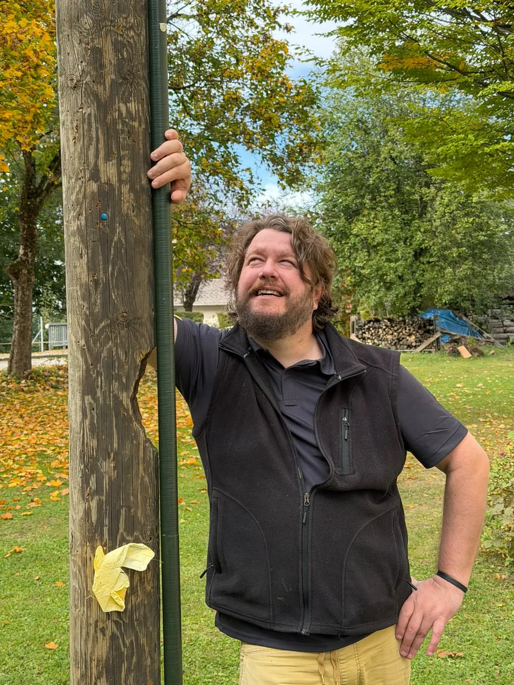 Lächelnder Funkamateur lehnt am Holzmast und blickt nach oben zur Antenne