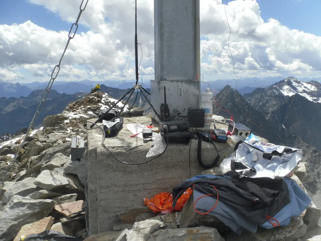 SOTA-Station am Gipfel des Roten Knopfs mit Handfunkgerät, Transceiver und Vertikalantenne vor verschneiten Bergen